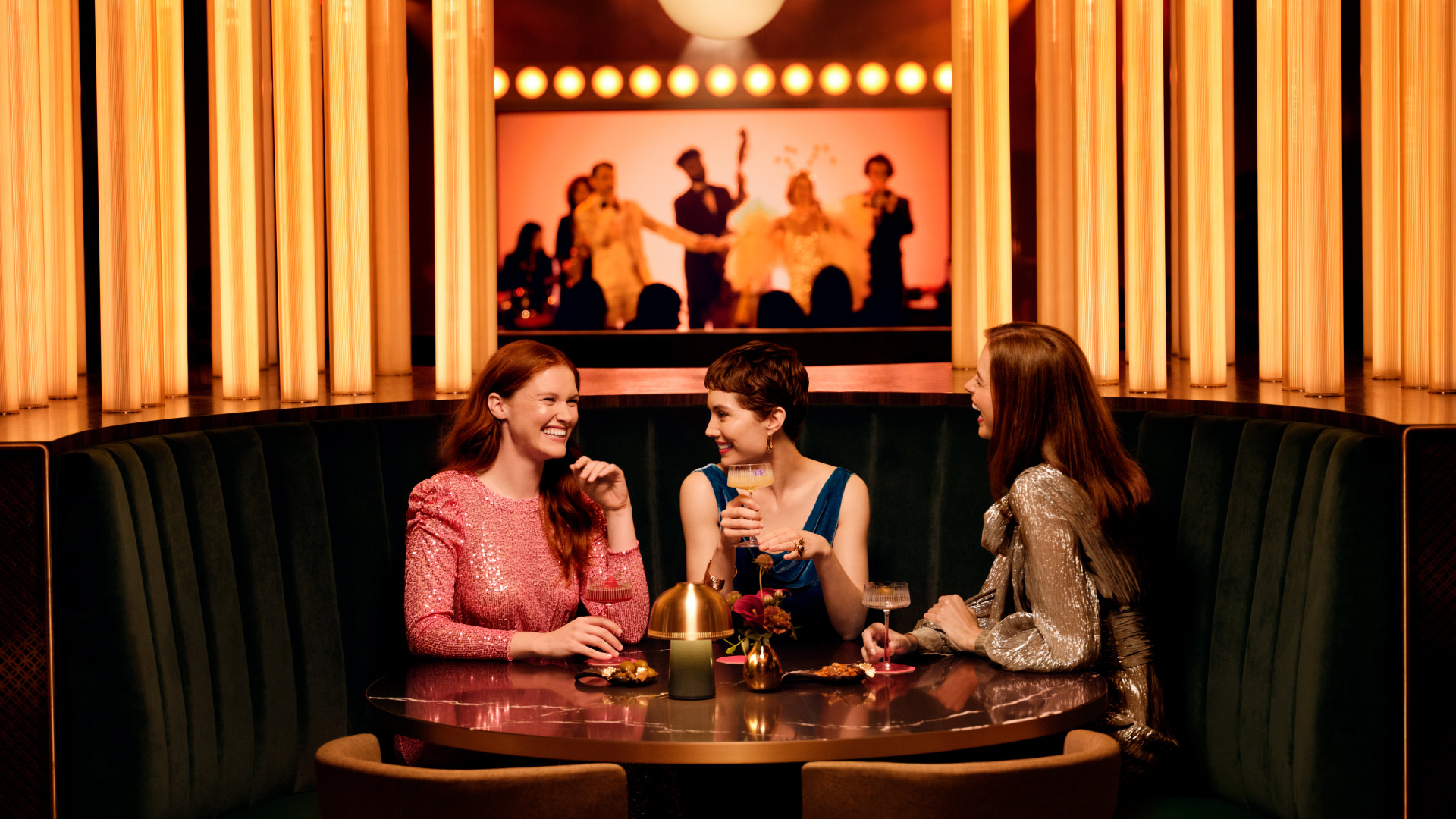 3 people sitting at a round booth dinner table, talking and laughing with each other.