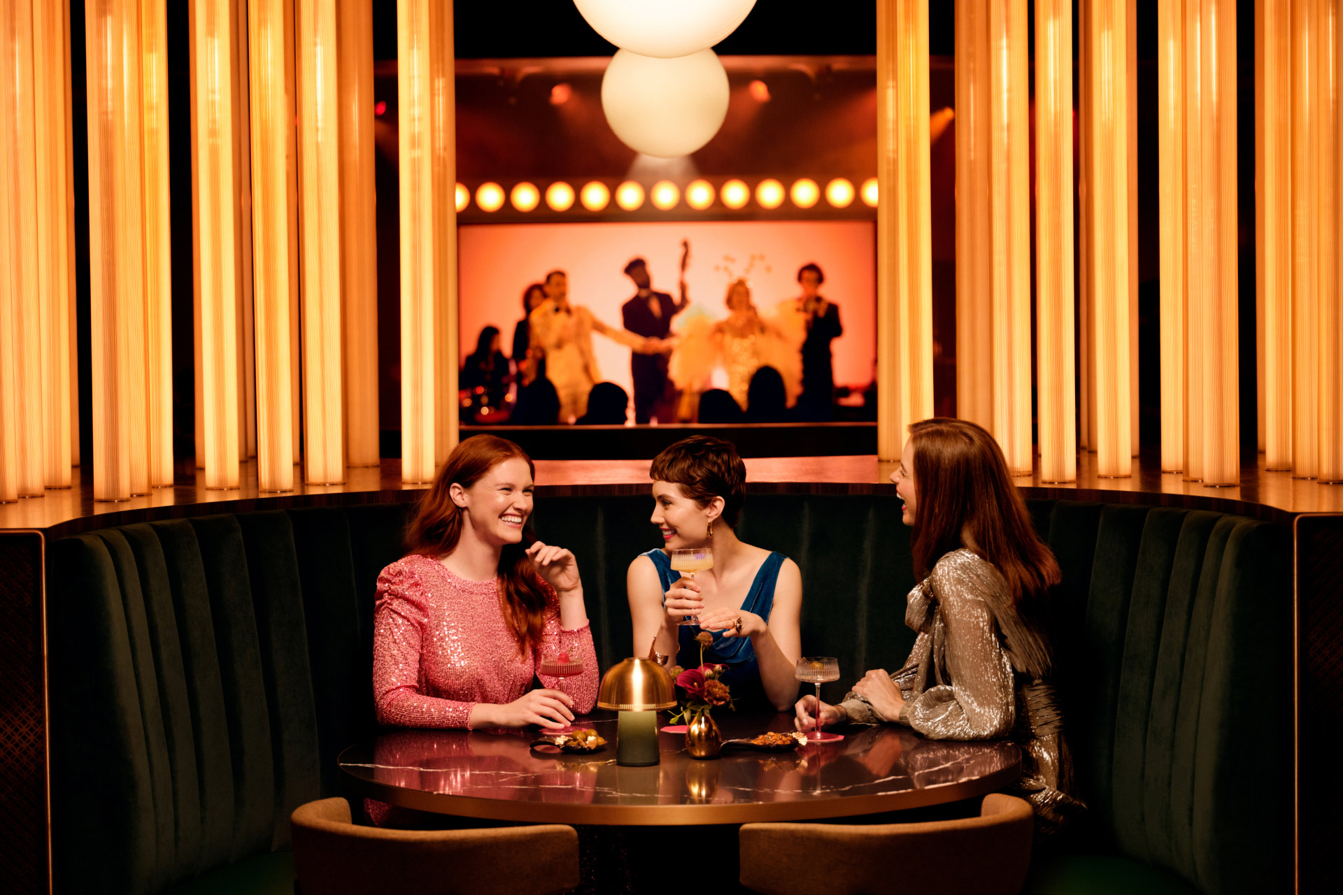 Open gallery overlay: three women enjoying drinks while a band plays in the background